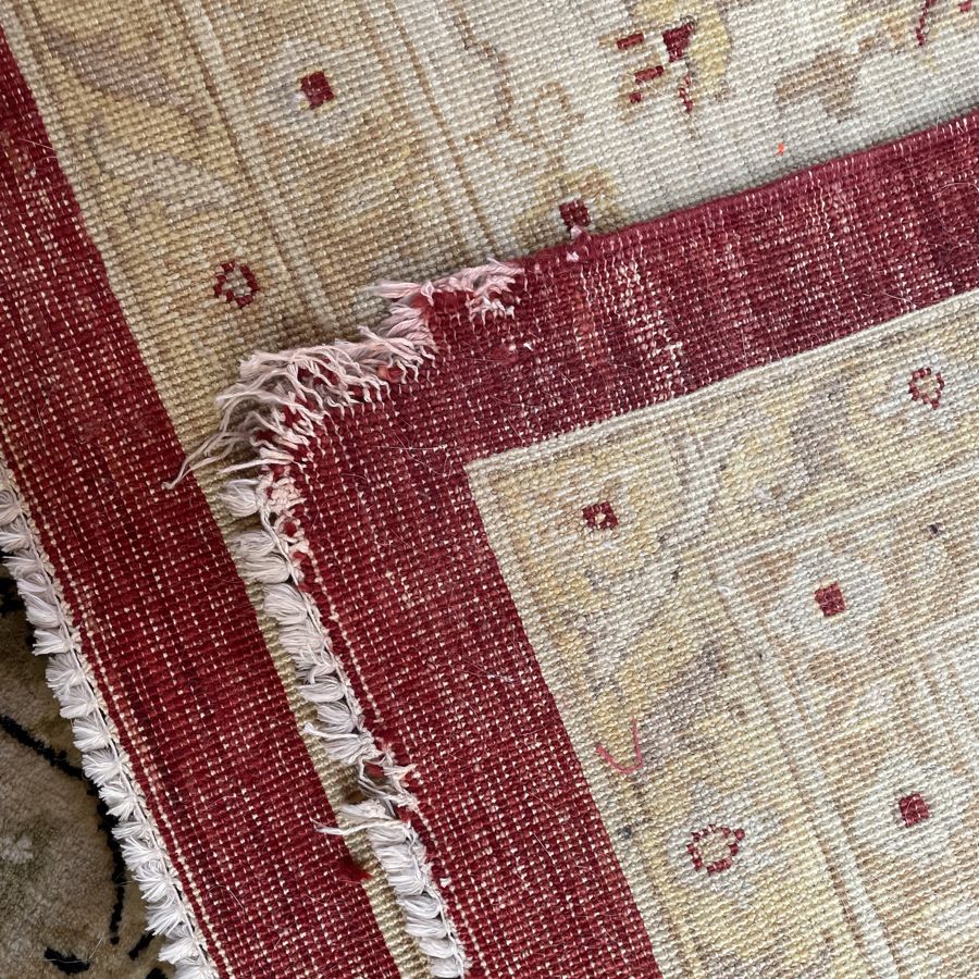 Ivory and red rug with a damaged corner and fringe