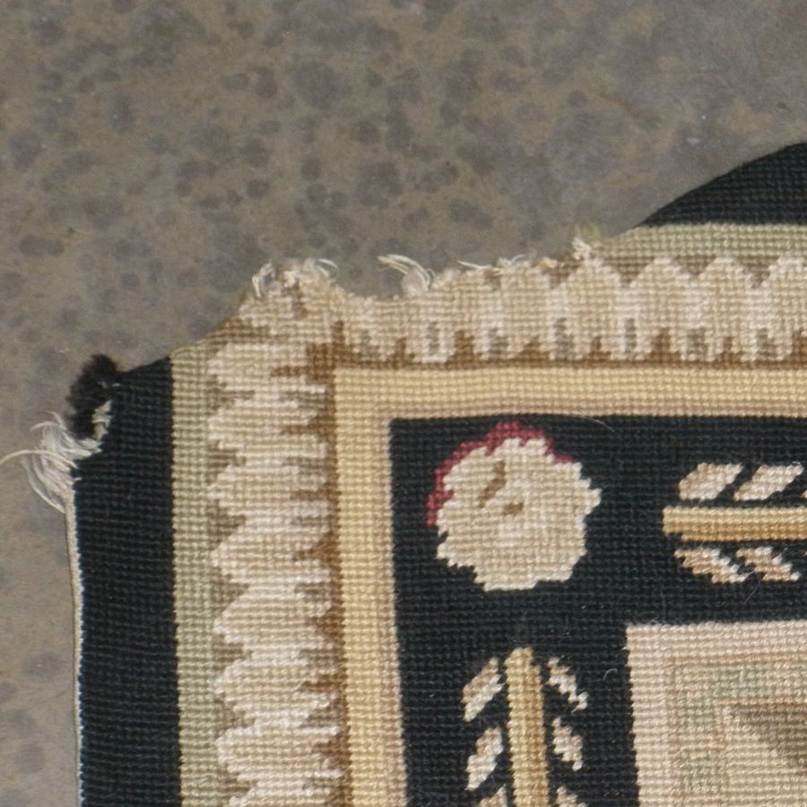 Needlepoint rug with a torn, frayed corner