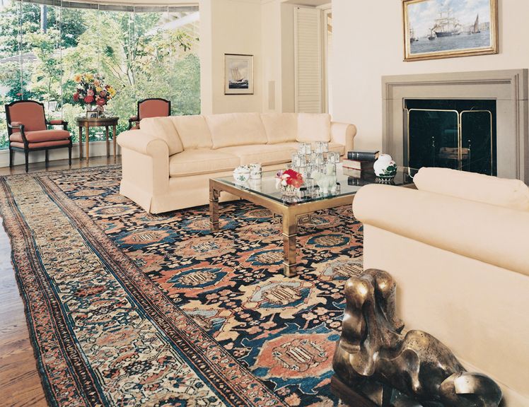 Large antique Persian rug in a bright living room with cream sofas and a fireplace